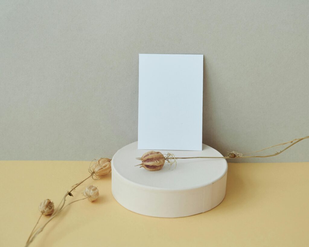 A simple mockup with dried flowers and a blank card on a cylindrical platform.